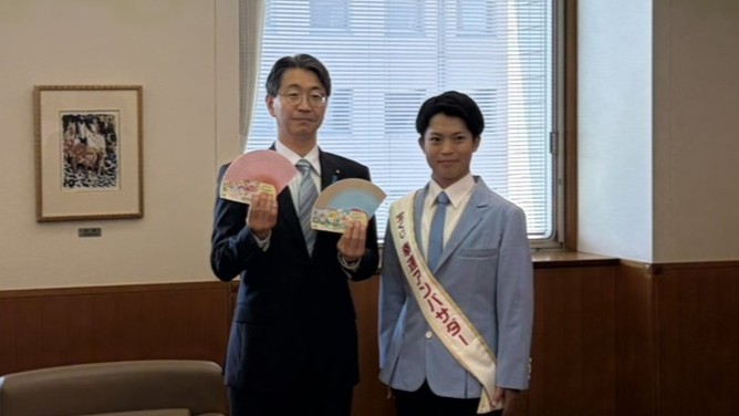 寺田副知事が宝くじの扇を広げたポーズで、「宝くじアンバサダー」篠原悠悟さんと並んでいる写真