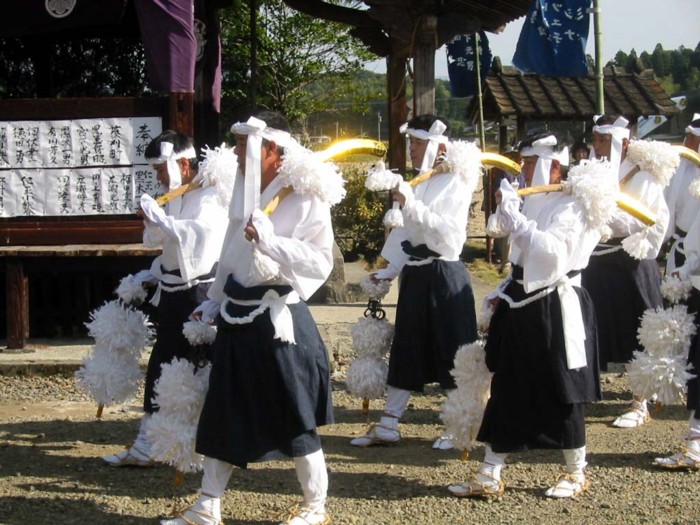 右手に錫杖，左手に鎌を持ち，うたっています