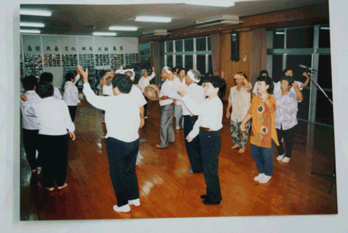 男性太鼓2名，踊り手2名を中心に女性が円陣を組んで歌い踊る